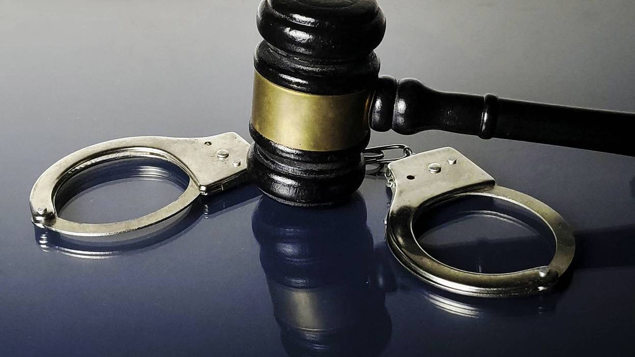 Wooden gavel and silver handcuffs on a reflective dark blue surface.