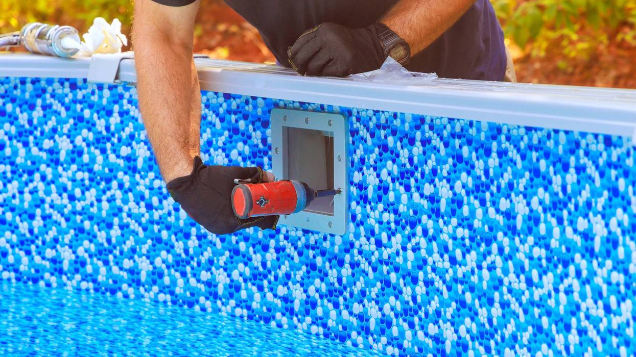 Worker performing maintenance on backyard swimming pool in sunny outdoor setting