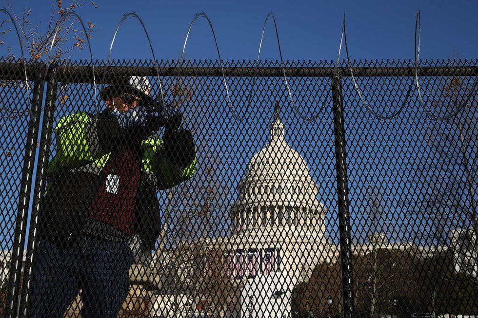 Workers put concertina razor wire along the top of the 8-foot