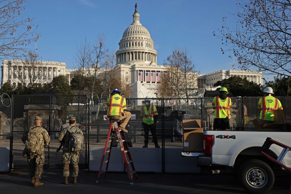 Workers put concertina razor wire along the top of the 8-foot