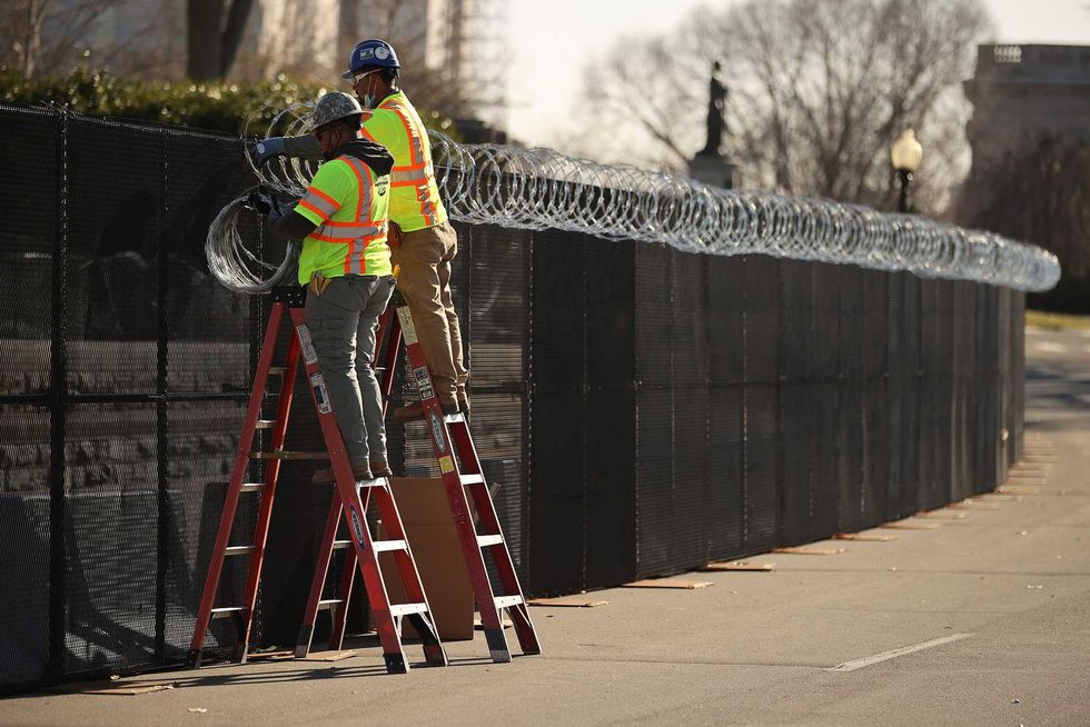 Workers put concertina razor wire along the top of the 8-foot