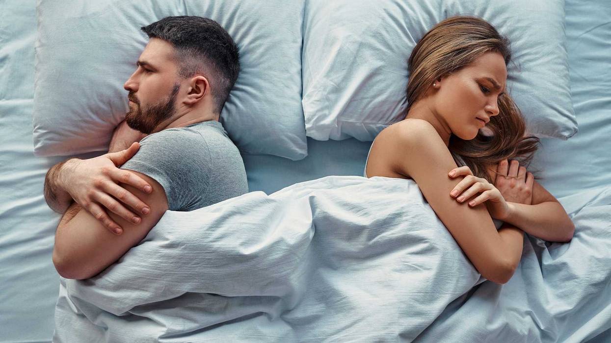 Young beautiful couple lying in bed turned back to back, arms crossed in anger and resentment. Relationship problems.Top view.