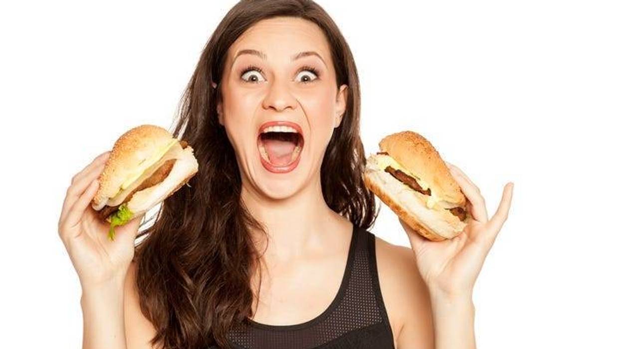 young beautiful greedy woman holding two burgers on white background