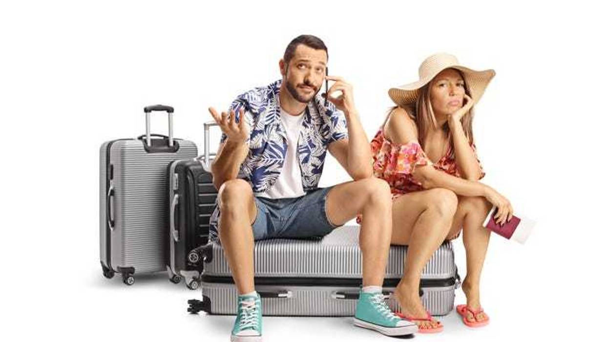 Young couple sitting on a suitcase and using a smartphone isolated on white background