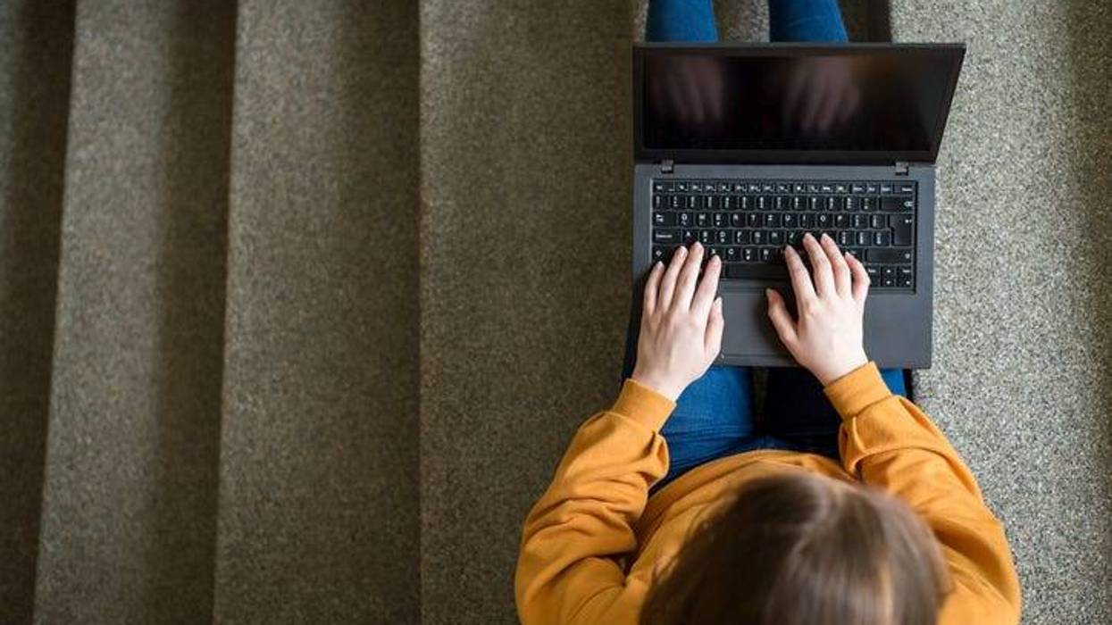 Young female college student sitting on stairs at school, writing essay on her laptop