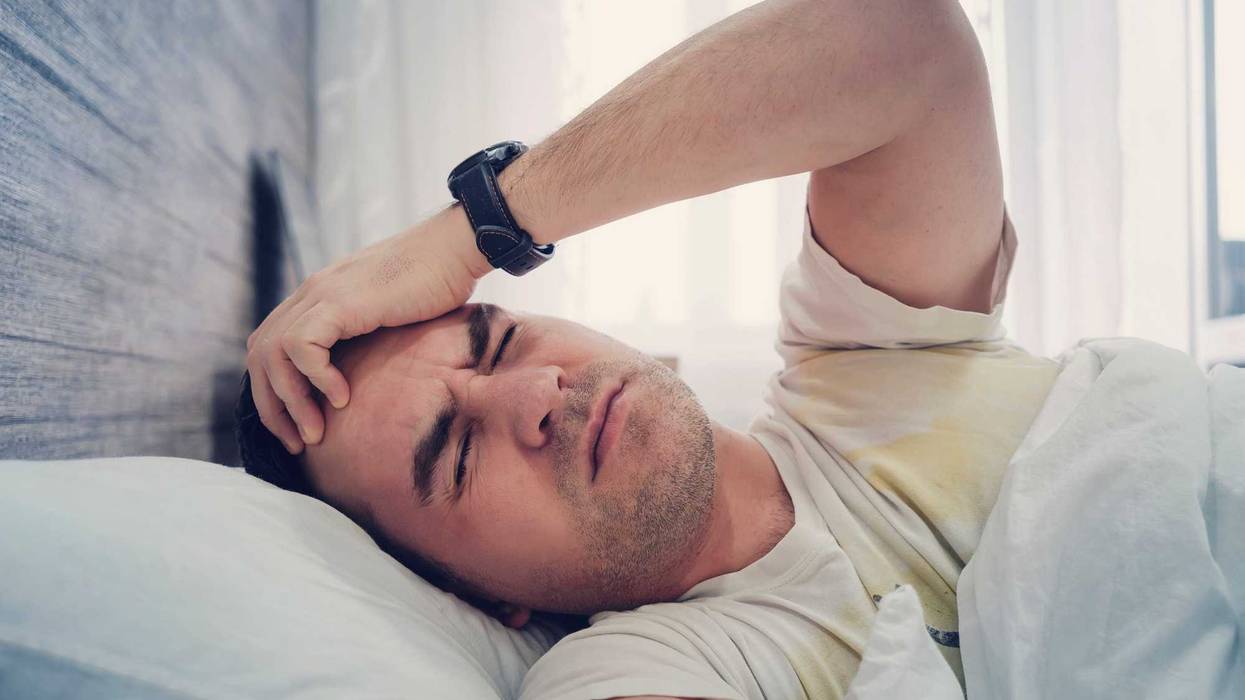 Young Man feel Headache in the Bed at the Home. an unslept guy is lying in bed with a dissatisfied emotion on his face. getting up early in the morning.