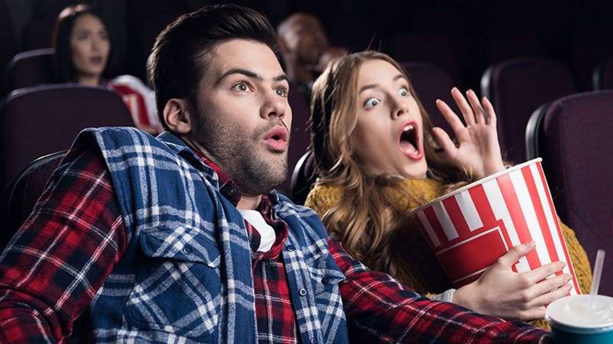 young shocked couple with popcorn watching movie in cinema