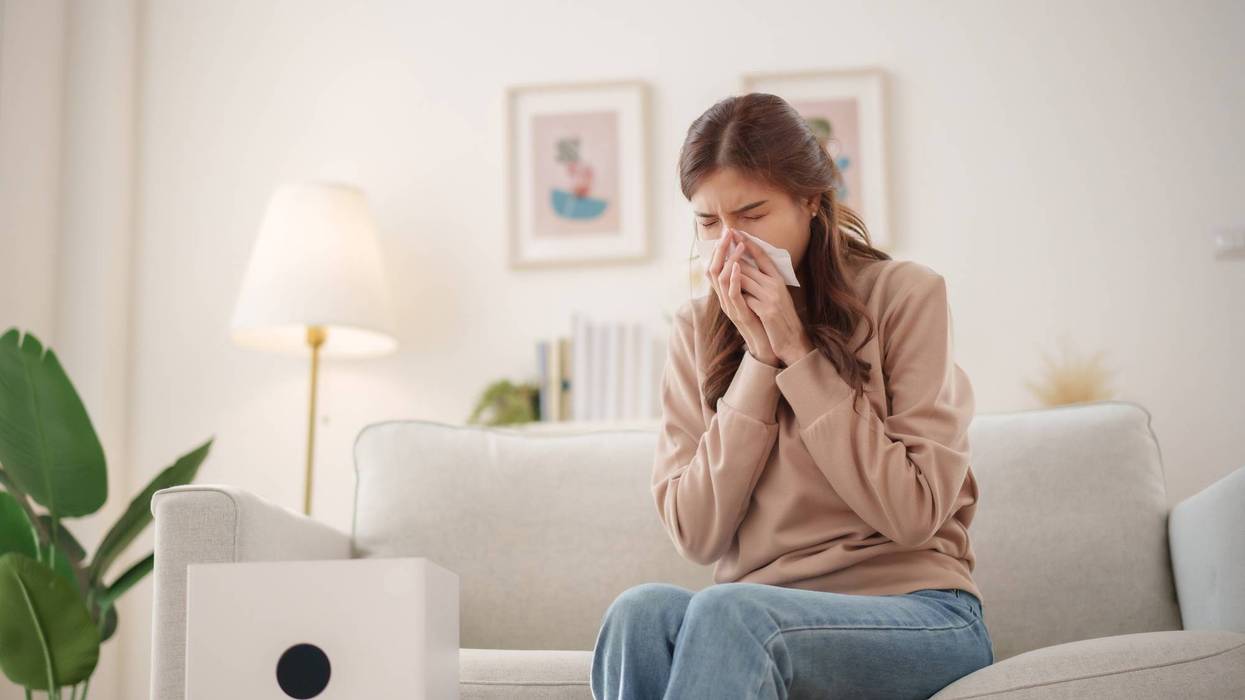 Young woman experiencing allergies at home with an air purifier in a bright, cozy living room