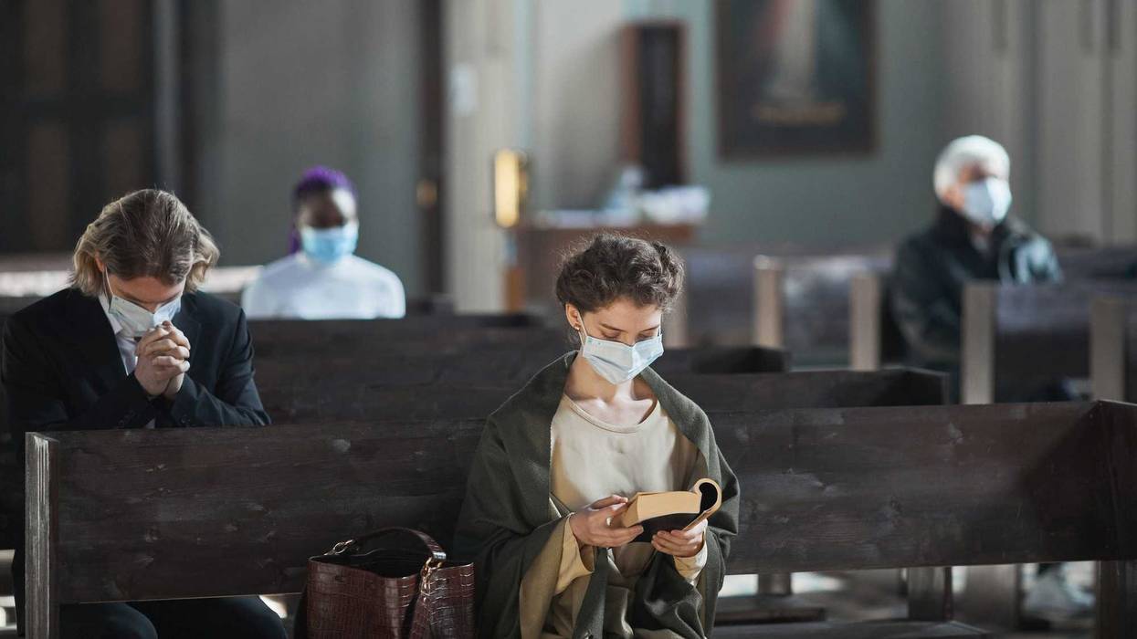 Young woman in protective mask sitting on bench and reading the Bible in the church