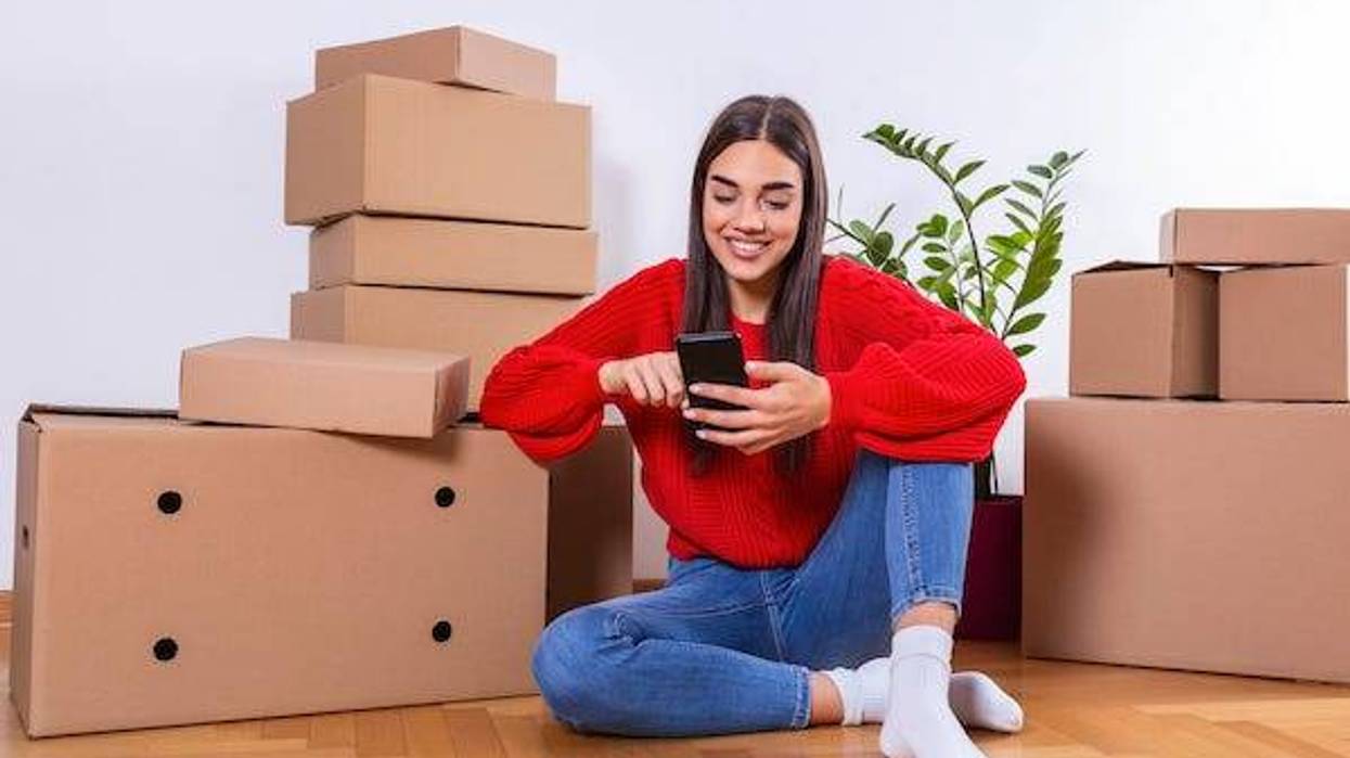 Young woman moving to a new apartment. Typing a message while sitting down