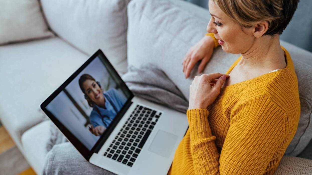 Young woman sitting on the sofa while talking with her doctor over a laptop.