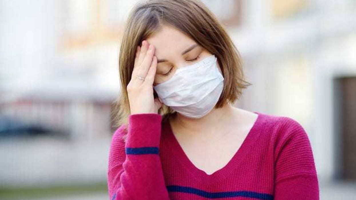 Young woman wearing a mask with a headache.