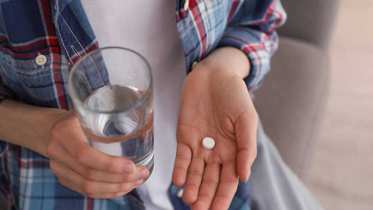 Young woman with abortion pill and glass of water indoors, closeup
