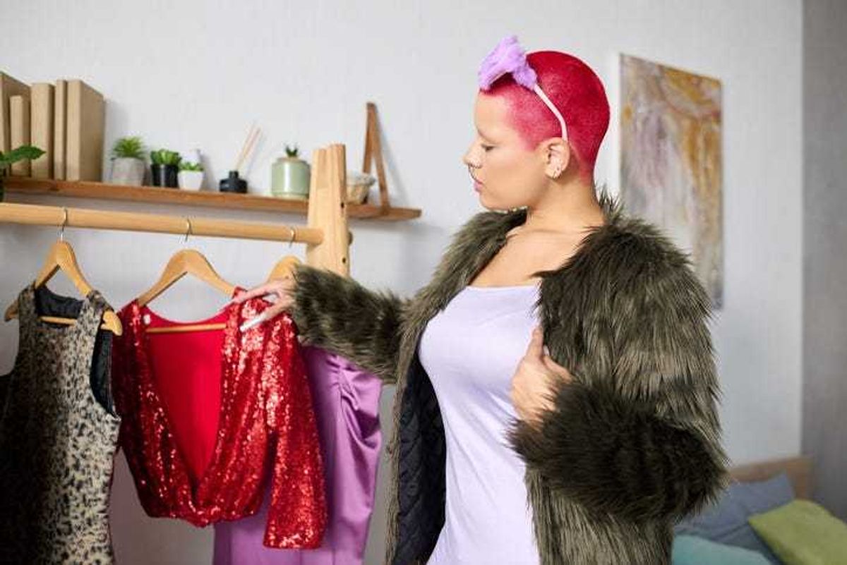 Young woman with pink hair considers outfits in her stylish modern apartment.