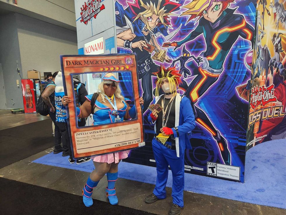 Yu-Gi-Oh! fans at New York Comic Con. One is dressed as the card Dark Magician Girl and the other is dressed as the character Yugi from the anime based on the card game.