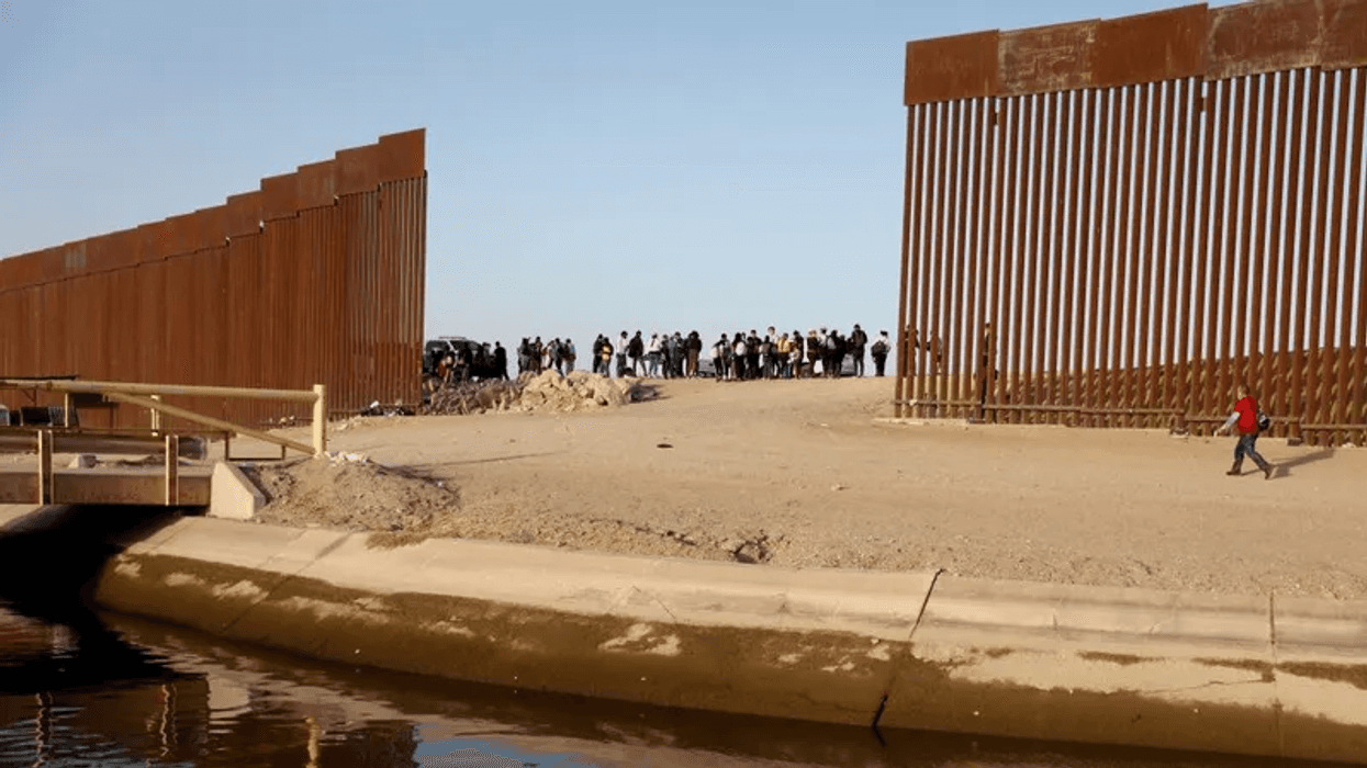 YUMA, ARIZONA- MAY 20: An immigrant (R) walks to cross through a gap in the U.S.-Mexico border barrier as others (C) await processing by the U.S. Border Patrol on May 20, 2022 in Yuma, Arizona