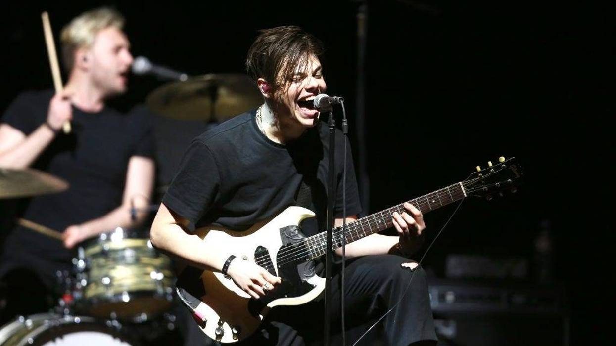 Yungblud plays guitar on stage with his trademark pink socks and giant smile.