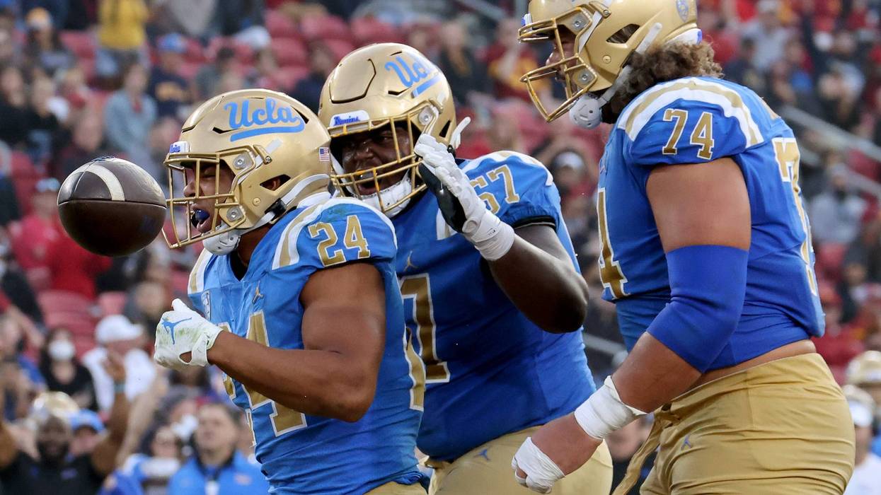 Zach Charbonnet #24 of the UCLA Bruins celebrates his touchdown run with Yutaka Mahe #67 and Sean Rhyan #74, to take a 48-26 lead over the USC Trojans, at Los Angeles Memorial Coliseum on November 20, 2021 in Los Angeles, California.